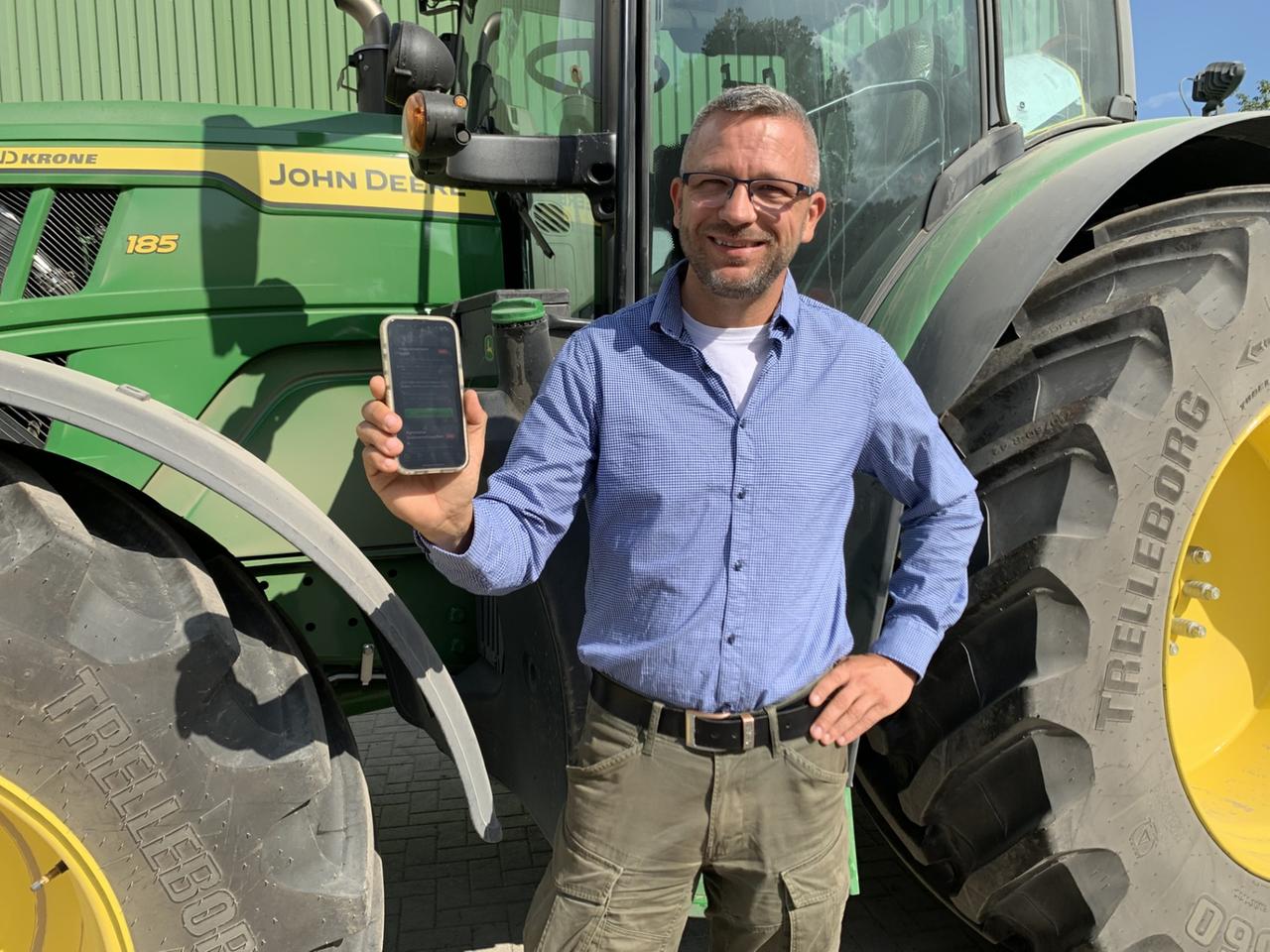 Landwirt vor John Deere Traktor mit App in der Hand